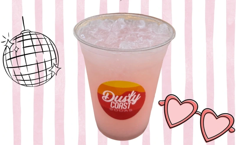 Pink Taylor Swift–themed soda in a Dusty Coast cup on a pink-striped background with disco ball and heart glasses.